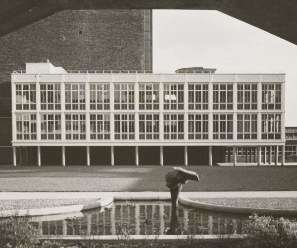 View of a modernist glass building in the medium distance, framed by an elevated concrete pedestrian bridge.