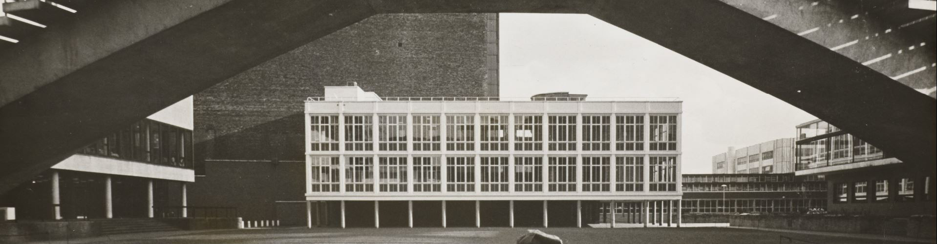 View of a modernist glass building in the medium distance, framed by an elevated concrete pedestrian bridge.