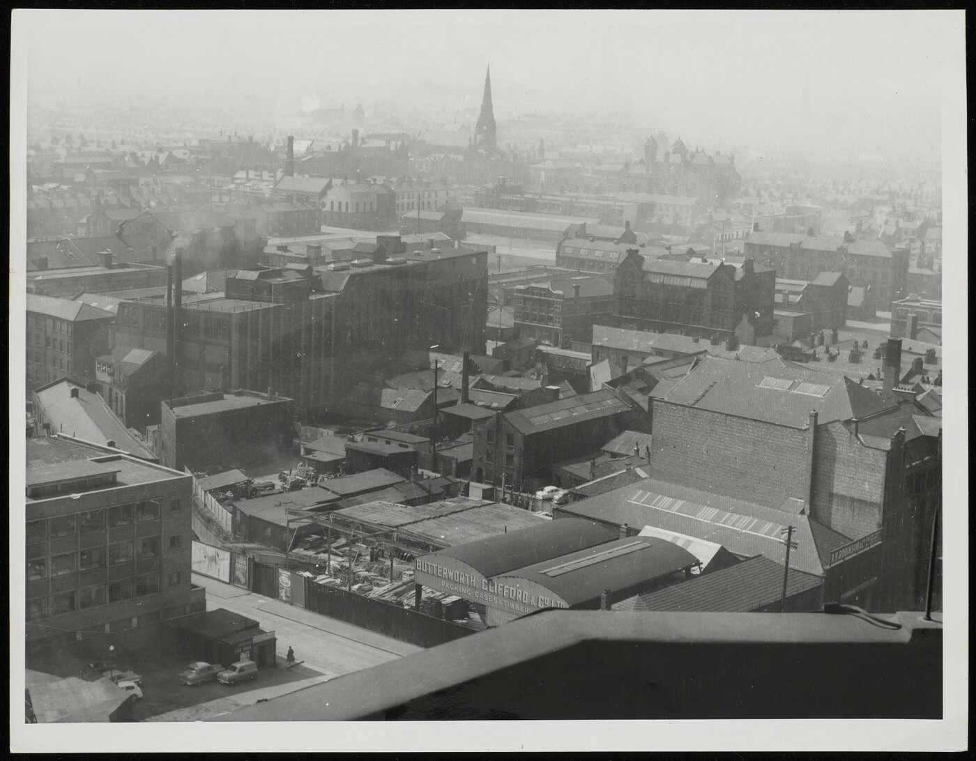 Aerial view of an area demolished to construct the UMIST campus, showing industrial buildings and warehouses, a timber merchants, and a church in the background. 