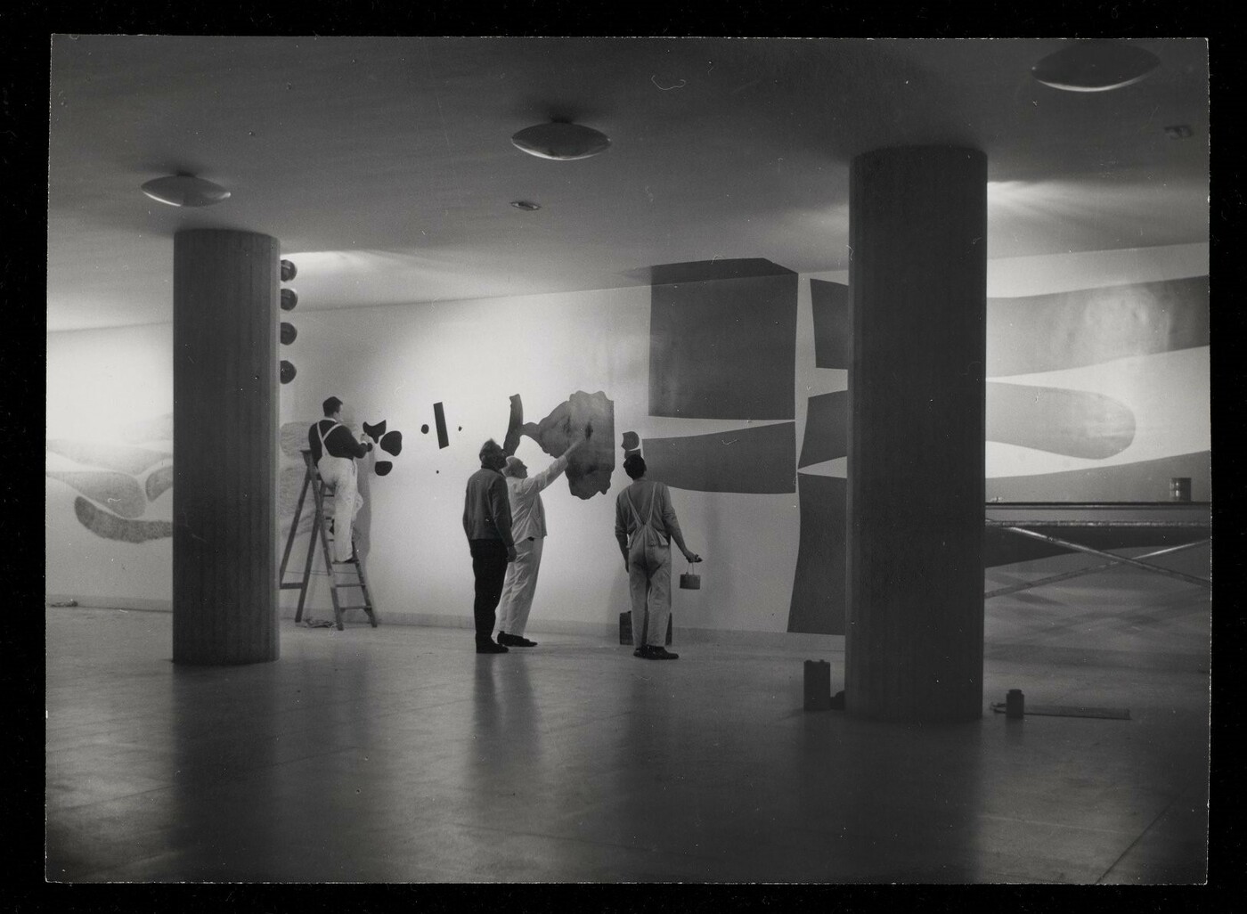 Mr Victor Pasmore (in dark clothes) directs the painting of his mural 'Metamorphosis' in the Renold Building, UMIST.