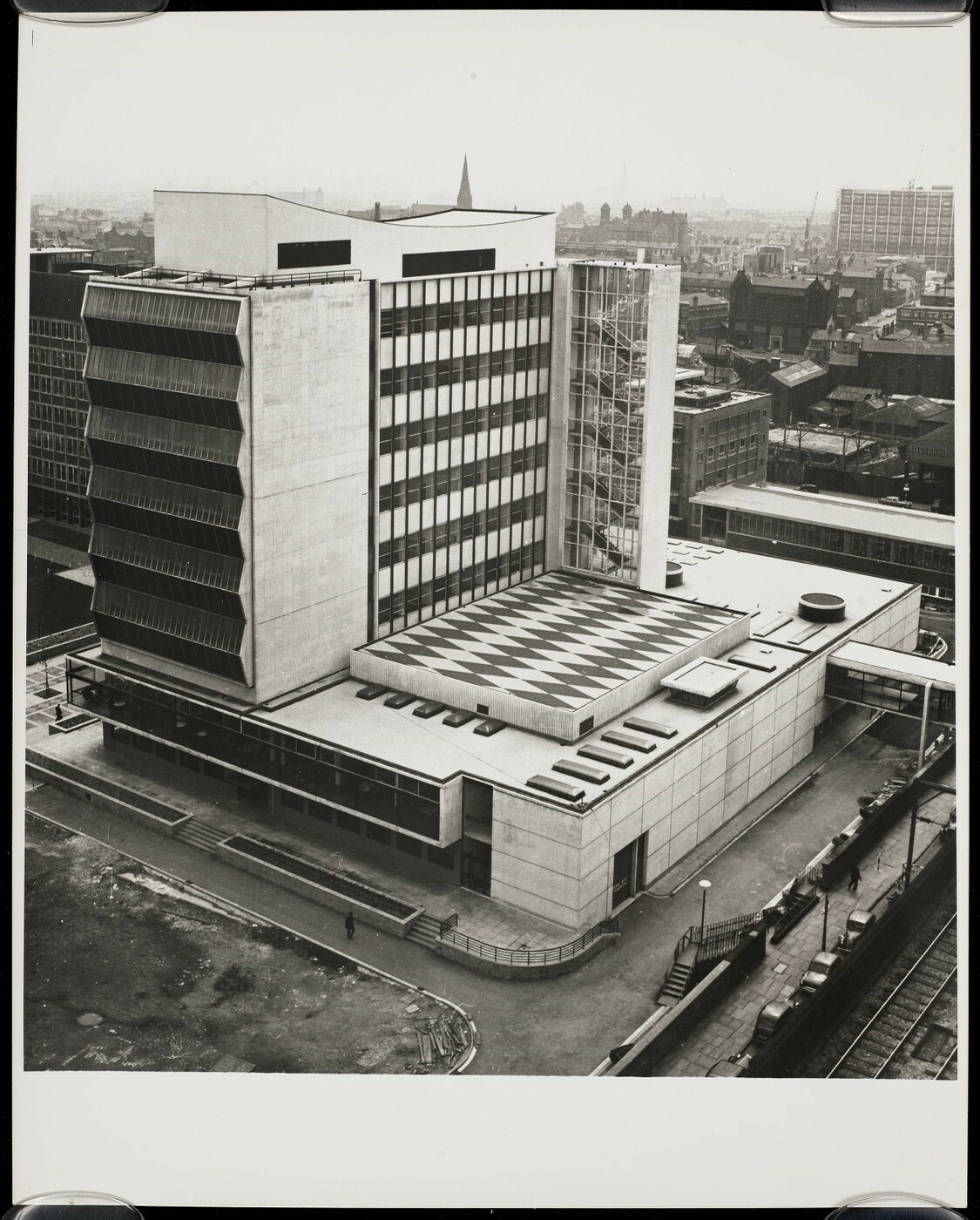 Monochrome photograph of the Renold building, a modernist tower block with a distinctive roof pattern.