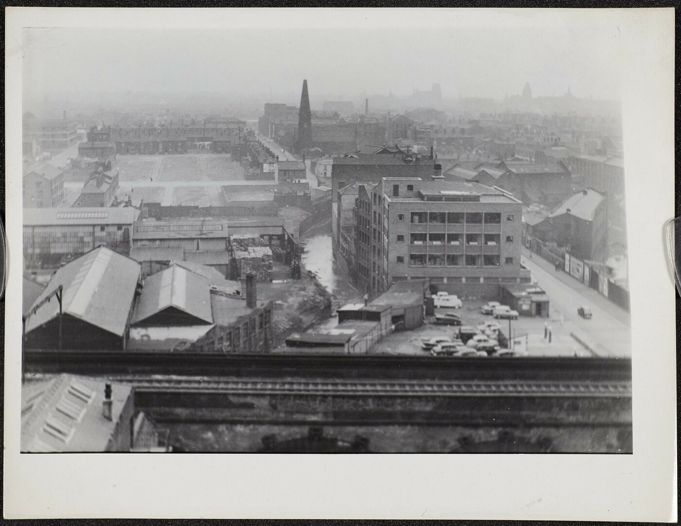 Aerial photograph showing industrial units in the foreground, cleared areas in the centre, and residential terraces with a church to the rear.