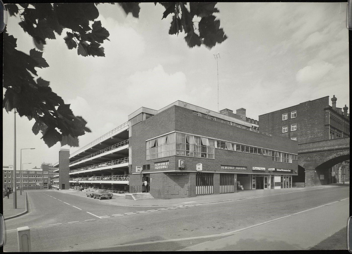 View of the Swinging Sporran pub and attached multi-storey car park  at a junction, with a railway bridge going over the road.