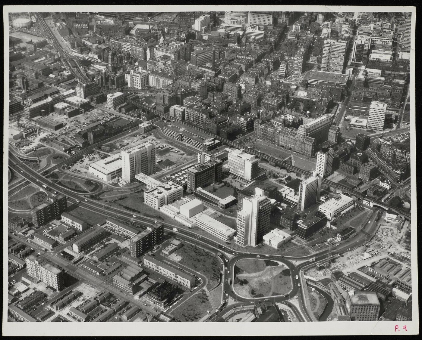 Aerial photograph showing the newly completed UMIST campus at the centre, among the Mancunian Way ring road, new residential units, and the Victorian buildings of central Manchester.  