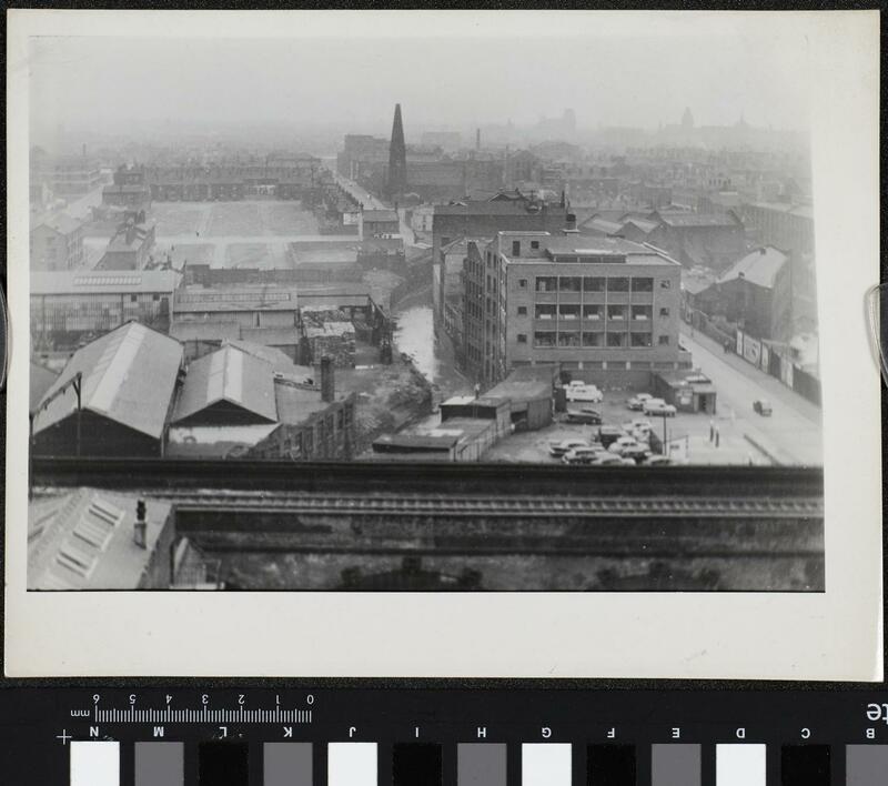 Aerial photograph showing industrial units in the foreground, cleared areas in the centre, and residential terraces with a church to the rear.