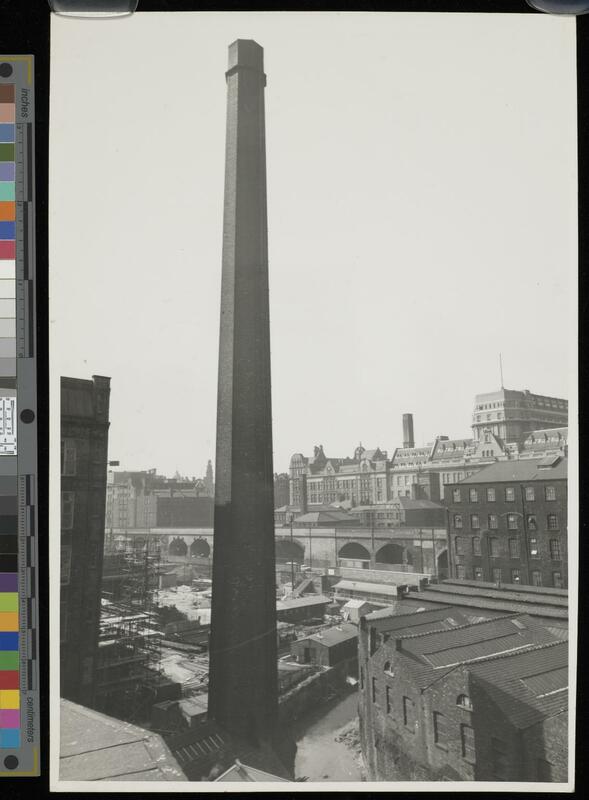 Large mill chimney in the foreground amidst industrial buildings, and the main UMIST building in the background.