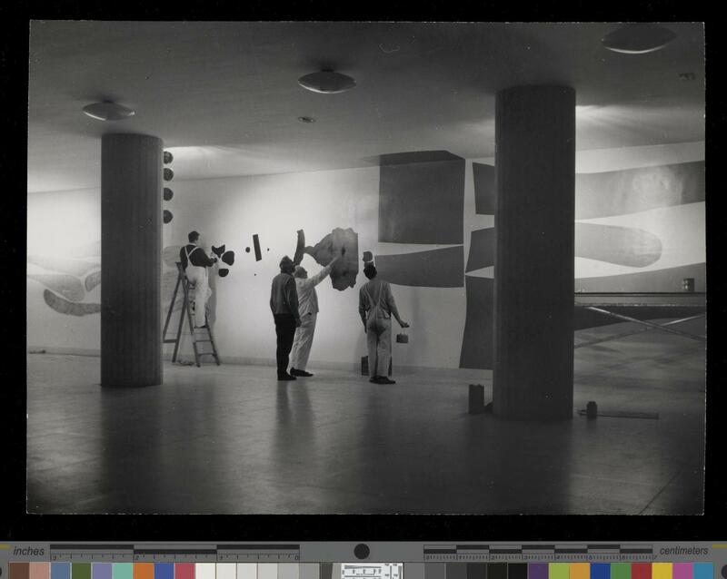 Mr Victor Pasmore (in dark clothes) directs the painting of his mural 'Metamorphosis' in the Renold Building, UMIST.