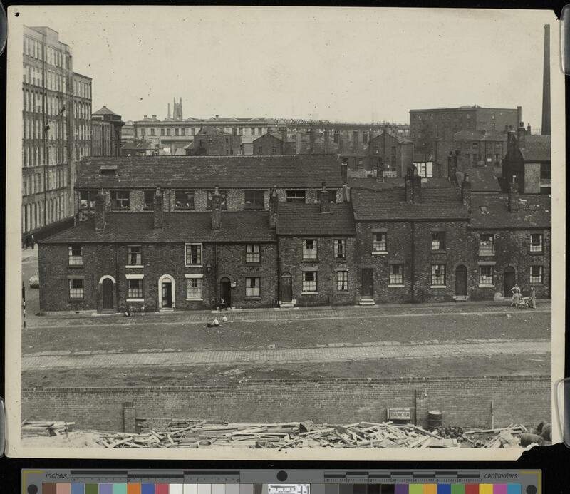 Rows of Victorian terraced housing in poor condition, with mills and warehouses in the background.