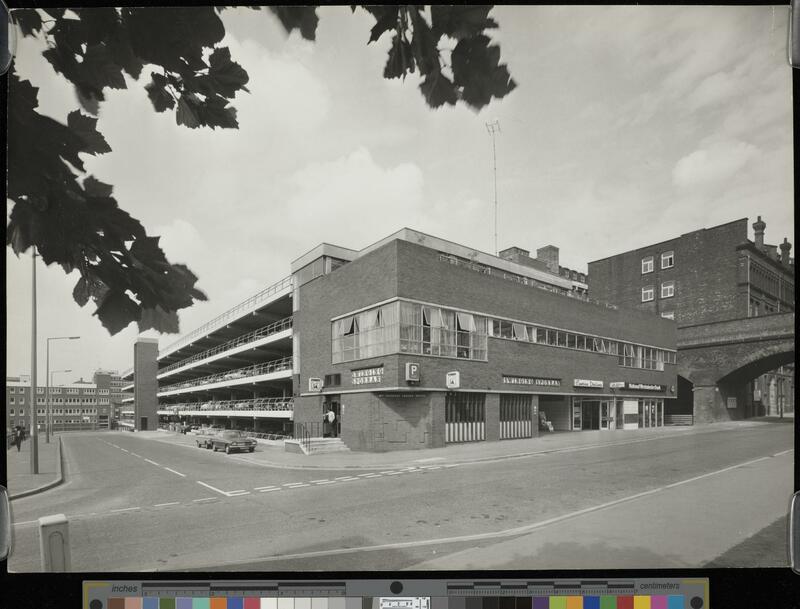 View of the Swinging Sporran pub and attached multi-storey car park  at a junction, with a railway bridge going over the road.