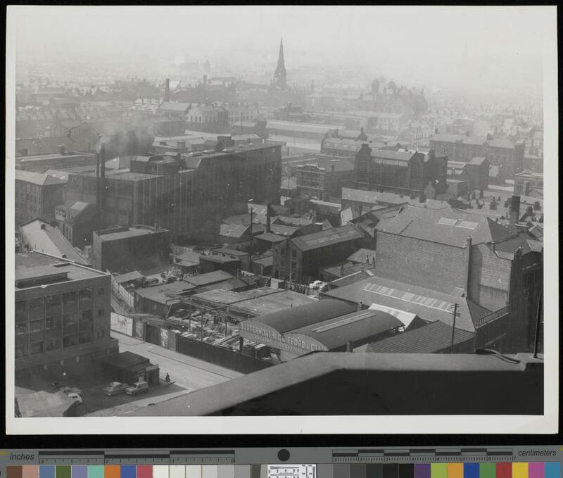 Aerial view of an area demolished to construct the UMIST campus, showing industrial buildings and warehouses, a timber merchants, and a church in the background. 